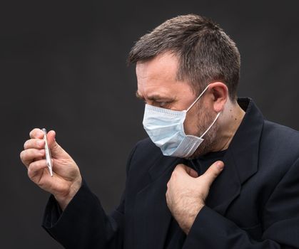 Illness. Man in medical mask with a thermometer