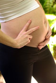 woman holding peace sign up with two fingers next to pregnant stomach