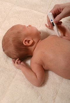 infant with fever and mother taking baby temperature with thermometer