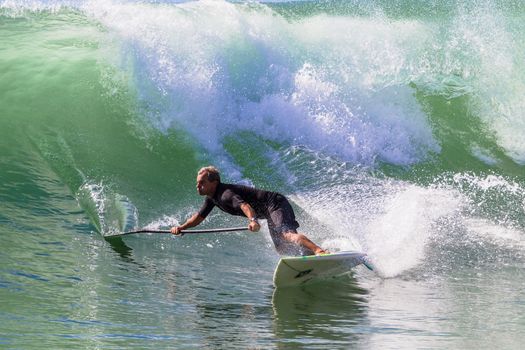 Surfer surfing turning riding sup board on good size clean wave.