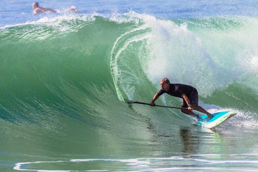 Surfer surfing bottom turns riding sup board on good size clean wave.