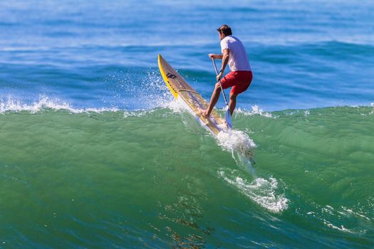 Surfer on sup board paddles over ocean wave