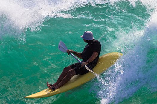 Paddle-ski rider drops down steep colorful wave to surf ride