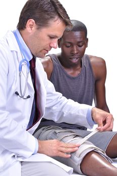 Male medical doctor secures leg brace on young black male athlete on white background