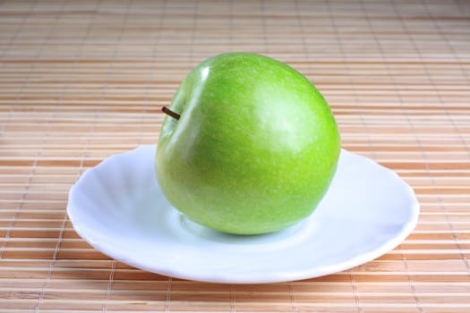 Green apple on the saucer at the wooden texture background