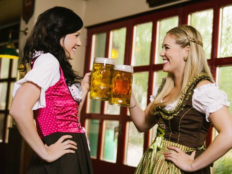 Photo of two beautiful woman wearing traditional dirndl and drinking beer.
