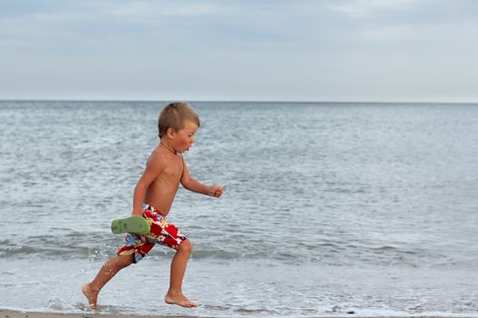 Little boy running at the shore near the sea