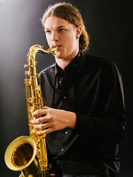 Photo of a young man playing the saxophone over dark background.
