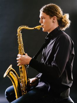 Photo of a young man playing the saxophone over dark background.
