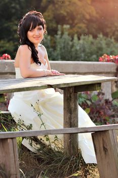 Girl in the wedding dress sitting on the bench neat the table