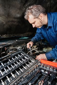 Photo of a mechanic repairing an engine of an old car.
