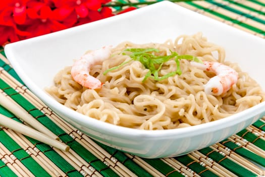 Composition of a bowl of noodles with shrimps on a bamboo table