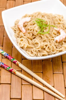 Composition of a bowl of noodles with shrimps on a wood table