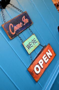 Come on in we're open sign on a blue painted wood door.