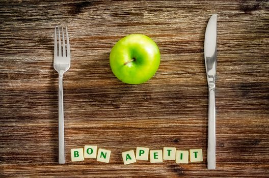 Silverware and apple on wooden vintage table with Bon apetit sign