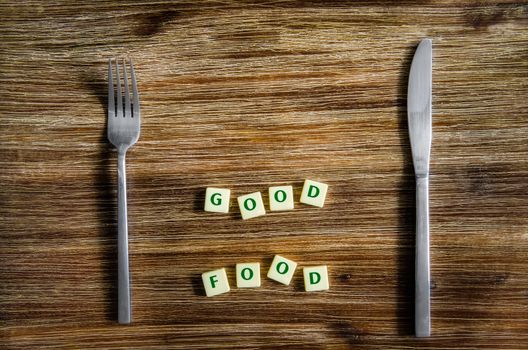 Knife and fork set on wooden vintage table with Good food sign