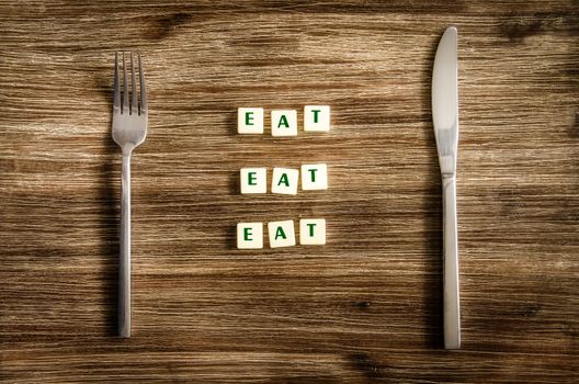Knife and fork set on wooden table with sign saying Eat, Eat, Eat