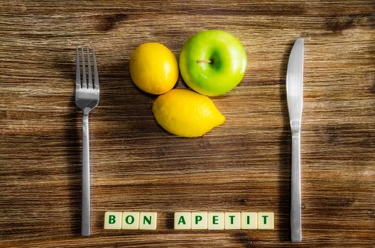 Lemons and apple on wooden vintage table with silverware and Bon apetit sign
