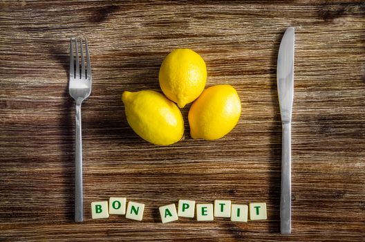 Silverware and lemons on wooden vintage table with Bon apetit sign