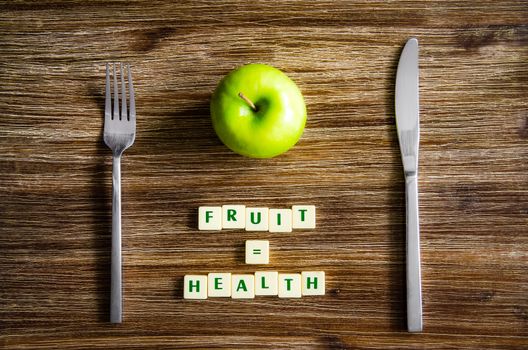 Silverware and apple set on wooden table with sign saying Fruit equals health