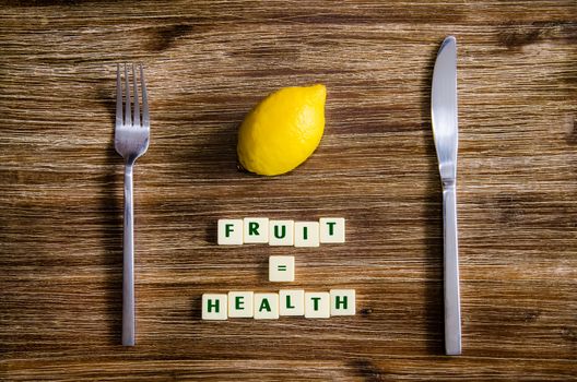 Silverware and lemon set on wooden table with sign saying Fruit equals health