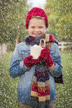 Handsome Young Boy Wearing Holiday Clothing Holding Hot Cocoa with Marshmallows and Candy Cane Outside in Light Snowfall.