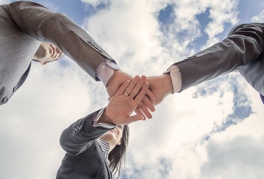 Bottom view of business team showing unity with hands together over blue sky background