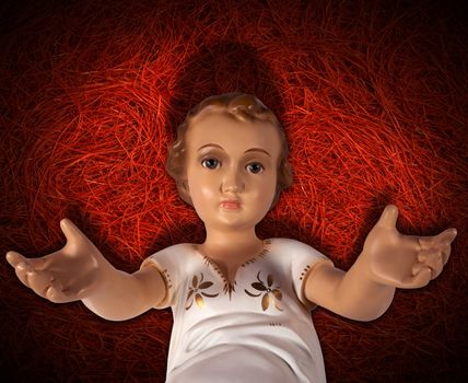 Baby Jesus figurine lying in manger on red straw background with shadows