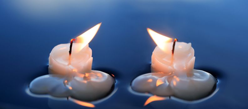 Two lighting candles on calm blue water