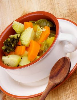 Rustic Vegetable Stew with Broccoli, Carrot, Leek and Potato in Beige Bowl with Wooden Spoon closeup on Wooden background