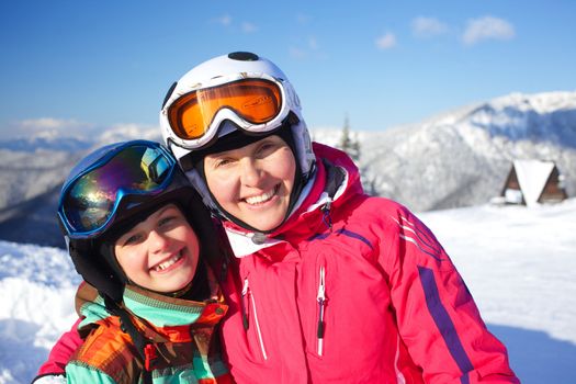 Portrait closeup of happy smiling girl in ski goggles and a helmet with his mother