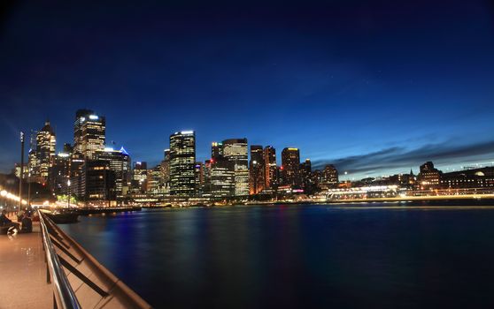 Sydney, Circular Quay, Australia - November 27, 2013; Nightscape scene of cityscape buildings aglow against a twilight sky and harbour reflections