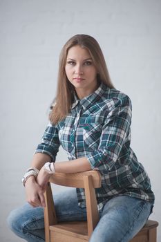 beautiful girl dressed in jeans and a shirt poses sitting on a chair