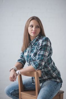 beautiful girl dressed in jeans and a shirt poses sitting on a chair