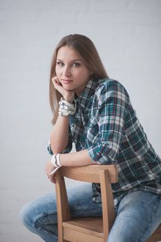 beautiful girl dressed in jeans and a shirt poses sitting on a chair