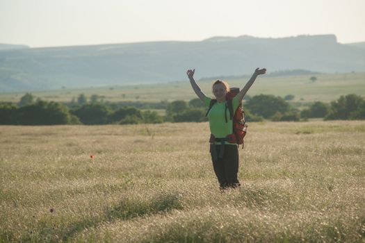 Happy smiling woman in field. Green grass in foreground and clear sky in background.
