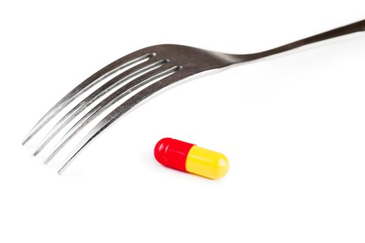 Closeup view of single capsule and fork over white background
