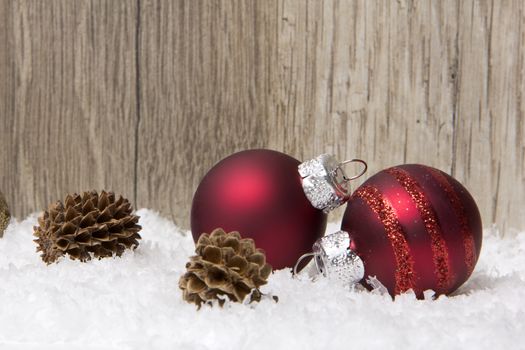 christmas decoration with wooden background, snow, christmas baubles red and pine cones 