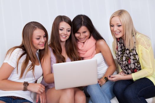 Group of beautiful young women sitting together on a couch sharing a laptop and smiling at something on the screen