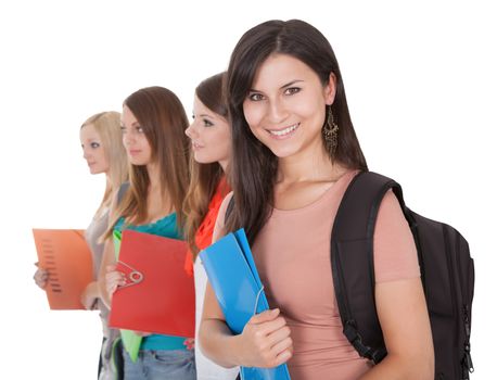 Four beautiful young female students standing in a receding row with folders of notes under their arms isolated on white