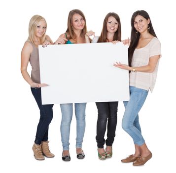 Studio shot of four attractive girls with a blank white board isolated on white