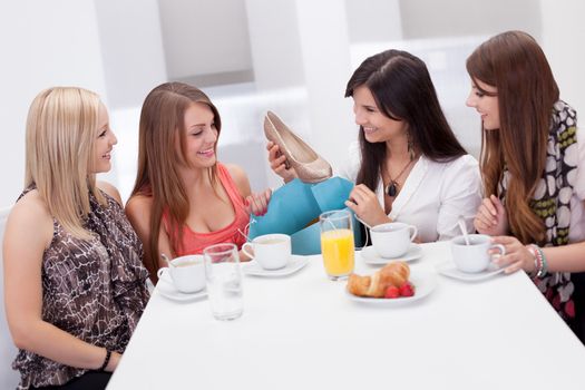 Women discussing footwear together seated at a morning coffee table as they compare their shopping purchases