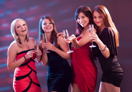 Group of four stylish women standing in a row toasting with flutes of champagne