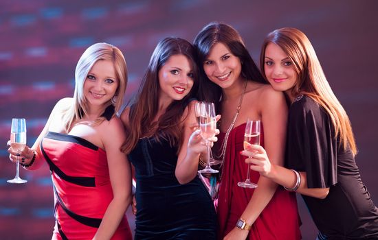 Group of four stylish women standing in a row toasting with flutes of champagne