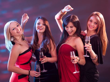 Group of four stylish women standing in a row toasting with flutes of champagne