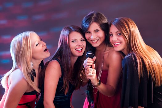 Four beautiful stylish girls singing karaoke at the club