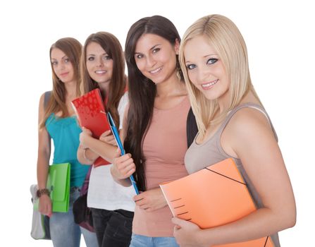 Four beautiful young female students standing in a receding row with folders of notes under their arms isolated on white