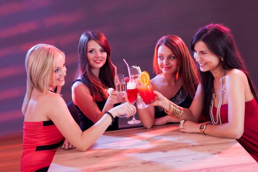 Four beautiful young female friends enjoying a cocktail seated at a table in a nightclub