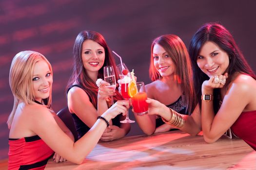 Four beautiful young female friends enjoying a cocktail seated at a table in a nightclub