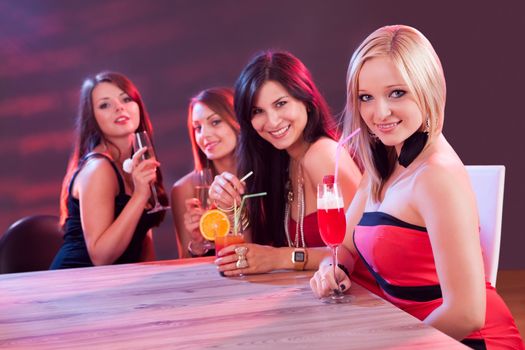 Female friends enjoying a night out sitting having cocktails at a table in a nightclub